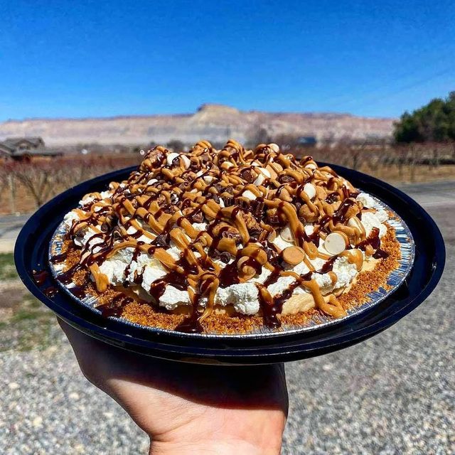 A whole cream pie with a piped topping, chocolate and caramel drizzle, almonds and chocolate chips.