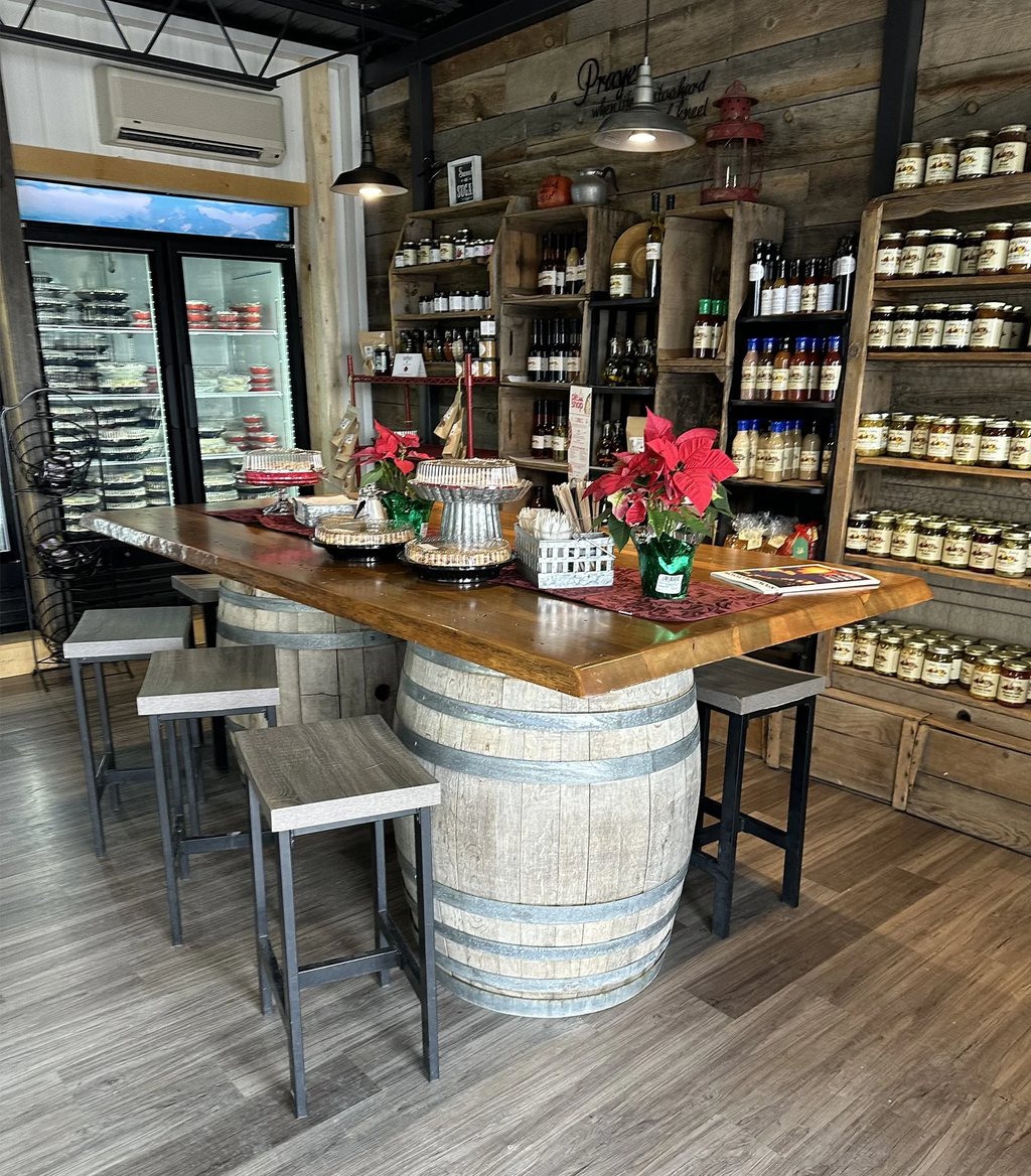 Inside Anita’s Pie Shop, with a barrel-base gathering table, shelves of preserves and the refrigerated pie case in view.