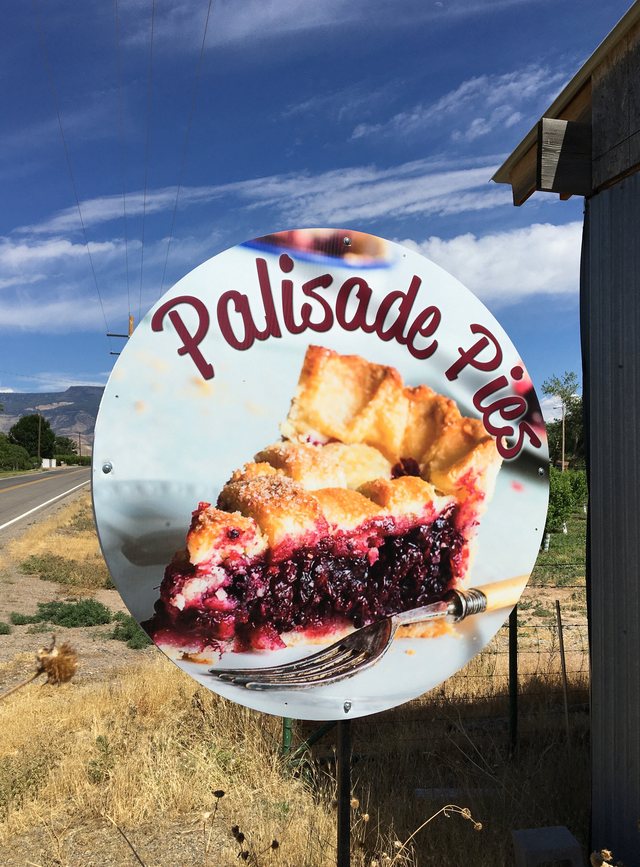 The roadside Palisade Pies sign beside C 1/2 Road with the mesa in the distance.